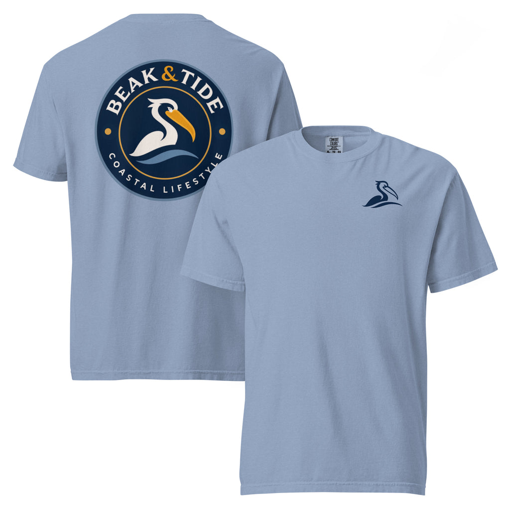 Product mockup of a washed denim short-sleeve t-shirt with a navy blue pelican logo on the left chest and a large circular 'Beak & Tide Coastal Lifestyle' graphic on the back. 